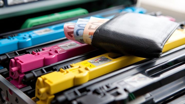 Druckerpatronen liegen in einem Drucker, w&auml;hrend ein Geldschein aus einem schwarzen Geldbeutel sichtbar herausragt.