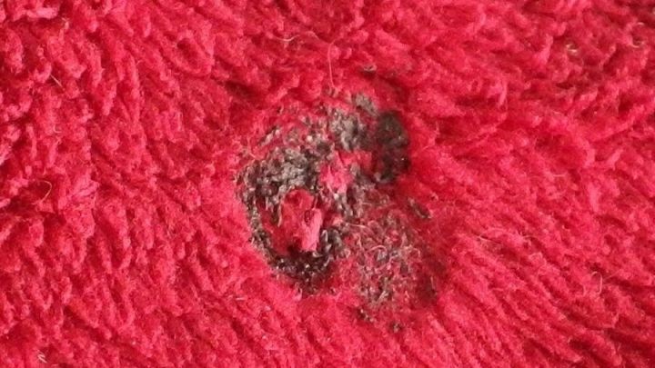 Ein rotes, kuscheliges Tuch mit einem Brandloch, das repariert werden soll, zeigt die besch&auml;digte Stelle deutlich.