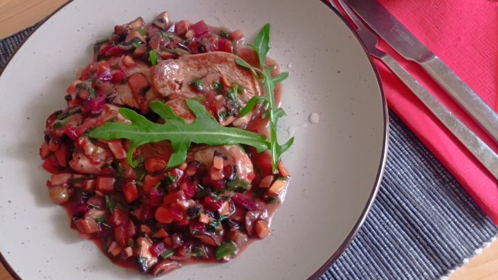 Saftige Kalbsfilet-Scheiben liegen auf einer bunten Gem&uuml;semischung, dazu Brezeln in einer Sch&uuml;ssel im Hintergrund.