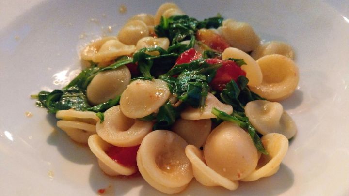 Orecchiette liegen in einem wei&szlig;en Teller und sind mit Rucola und kleinen Tomaten vermischt.