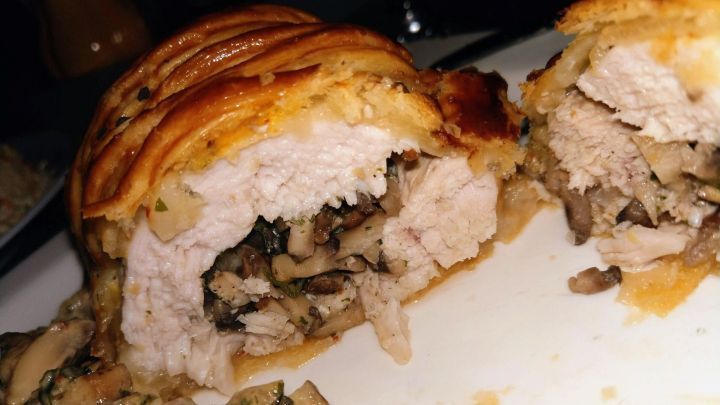 Gef&uuml;llte H&auml;hnchenbrust in Bl&auml;tterteig, frisch aufgeschnitten, pr&auml;sentiert sich auf einem Teller mit einer cremigen So&szlig;e daneben.