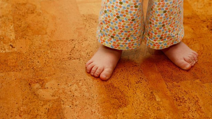Ein Kind steht barfu&szlig; auf einem Korkboden, dessen warme, nat&uuml;rliche Textur den Raum gem&uuml;tlich wirken l&auml;sst.