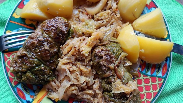 Auf einem bunten Teller liegen Gr&uuml;nkohl-Rouladen, umgeben von Wei&szlig;kohl und Kartoffeln, die zum Essen bereit sind.