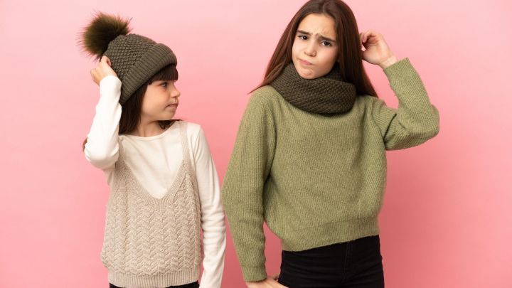 Zwei M&auml;dchen stehen vor einem rosa Hintergrund; sie zeigen unterschiedliche Gef&uuml;hle und tragen Winterkleidung.