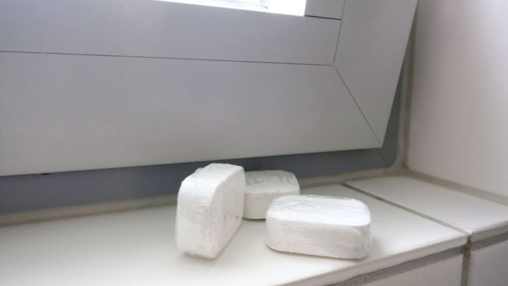 Drei Sp&uuml;lmaschinentabs liegen auf einer wei&szlig;en Fensterbank neben einem sauberen Fensterrahmen.