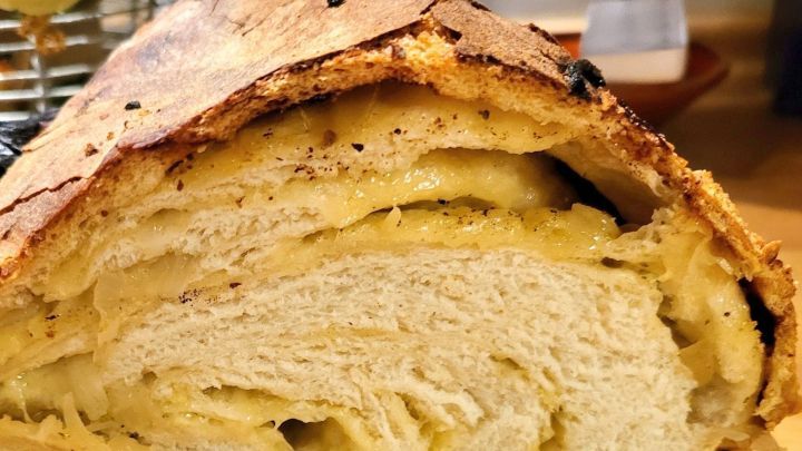 Ein frisch aufgeschnittenes K&auml;se-Zwiebel-Brot zeigt die schmelzende F&uuml;llung zwischen weichem Teig auf einem Holzbrett.