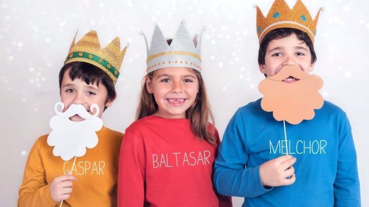 Drei Kinder in bunten Shirts und Kappen stellen die Heiligen Drei K&ouml;nige dar, l&auml;cheln und halten Requisiten in der Hand.