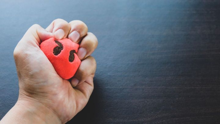 Eine Hand dr&uuml;ckt einen roten Stressball mit Augen zusammen, w&auml;hrend er auf einem dunklen Tisch liegt, um Stress abzubauen.
