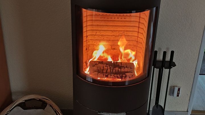 Ein moderner Kamin steht in einem Raum und gibt warmes Licht ab, w&auml;hrend Holzscheite darin brennen.