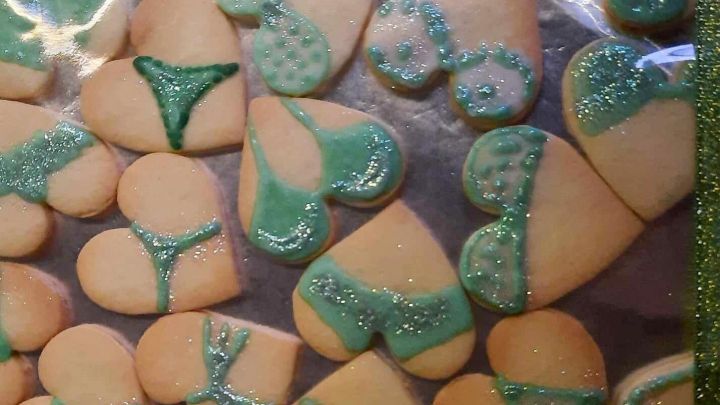 Herzf&ouml;rmige Pl&auml;tzchen mit gr&uuml;ner Zuckerglasur sind auf Plastikfolie angerichtet, dekoriert in sexy Dessous-Designs.