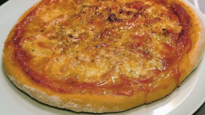 Auf einem wei&szlig;en Teller liegt eine knusprige Pizza mit goldbraunem K&auml;se und Tomatensauce, frisch zubereitet zu Hause.