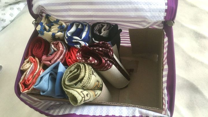 Ordentlich gerollte Halst&uuml;cher sind in einer gepunkteten Tasche verstaut, die auf einem Bett liegt.