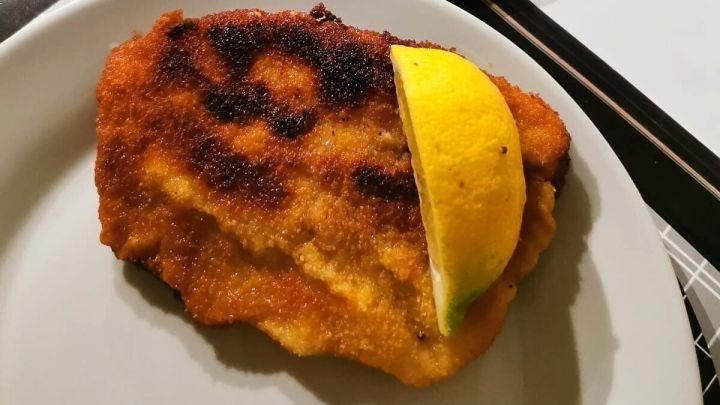 Ein paniertes Schnitzel liegt auf einem Teller, garniert mit einer Scheibe Zitrone, neben einem hohen Berg Pommes frites.