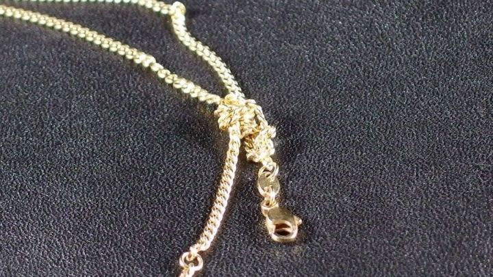 Ein goldfarbenes Schmuckkettchen mit einem Knoten liegt auf einem dunklen Untergrund, w&auml;hrend es gel&ouml;st wird.