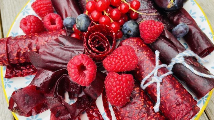 Auf einem Teller liegt buntes Fruchtleder, das in verschiedenen Formen und Farben angeordnet ist, umgeben von frischen Beeren.