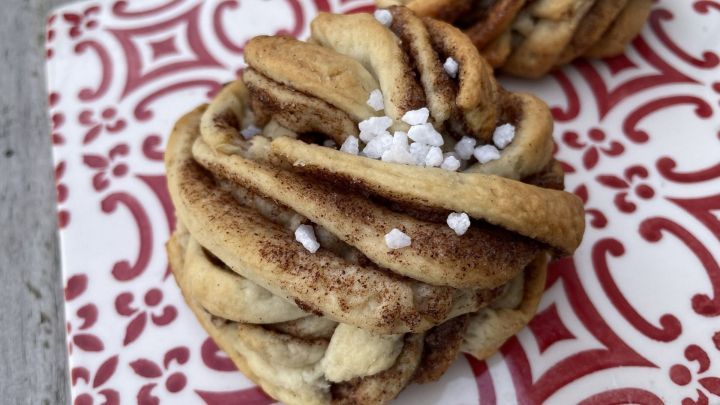 Zimtknoten liegen auf einem dekorativen Teller und sind mit Zucker bestreut, umgeben von einem rustikalen Holzuntergrund.