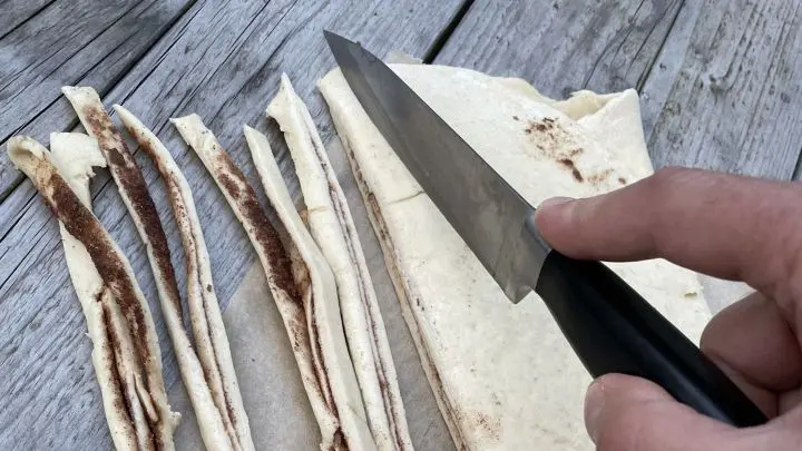 Der gefaltete Hefeteig mit Zimtf&uuml;llung wird f&uuml;r die Zimtknoten in Streifen geschnitten.