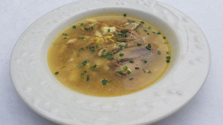 Eine Sch&uuml;ssel mit klarem Suppenbr&uuml;he, gef&uuml;llt mit Suppenhuhn und frischen Kr&auml;utern, steht auf einer frostigen Unterlage.