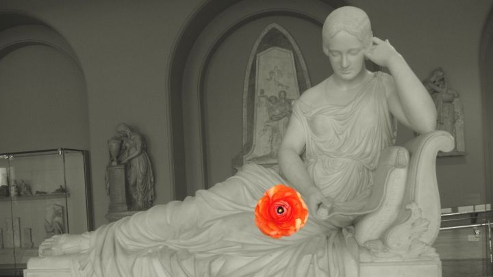 Eine Statue einer weiblichen Figur liegt entspannt, h&auml;lt eine leuchtende Blume w&auml;hrend sie in einem Museum ausgestellt ist.