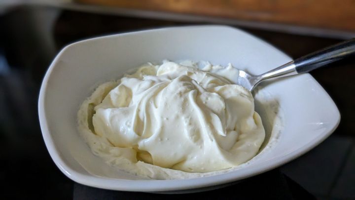 Eine Sch&uuml;ssel mit cremiger Cr&egrave;me fra&icirc;che steht auf einem Tisch, w&auml;hrend ein L&ouml;ffel bereitliegt, um sie zu servieren.