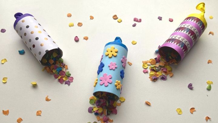 Bunte Konfettikanonen liegen auf einem Tisch und sind mit Pappe verziert, w&auml;hrend Konfetti herausf&auml;llt.