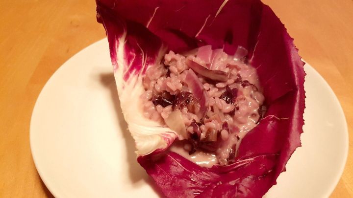 Ein Radicchio-Blatt h&auml;lt cremiges Risotto, das mit lila und wei&szlig;en Reisst&uuml;cken gef&uuml;llt ist, auf einem wei&szlig;en Teller.