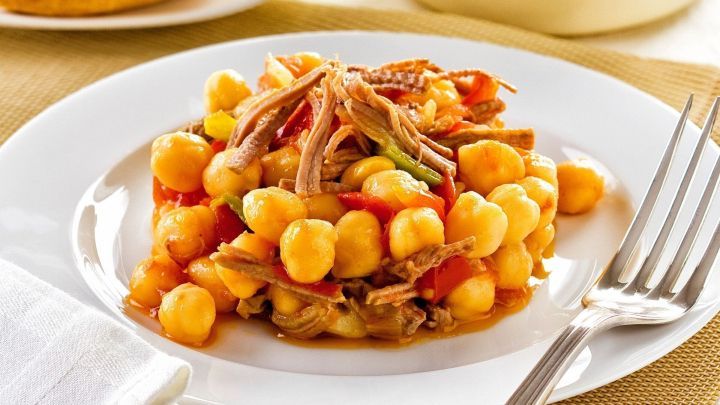 Ein Eintopf aus Kichererbsen und Fleisch liegt auf einem wei&szlig;en Teller, umgeben von einem rustikalen Tischsetting.