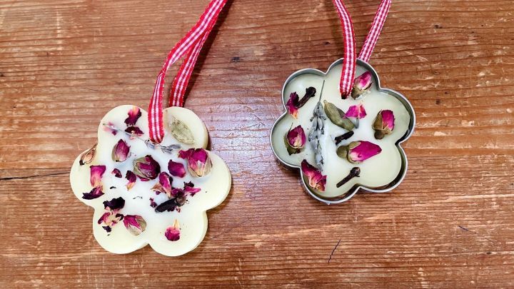 Zwei s&uuml;&szlig;e Duftanh&auml;nger aus Wachs h&auml;ngen an gestreiften B&auml;ndern, umgeben von rustikalem Holz.