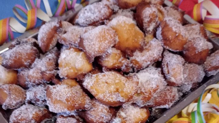 Ein Blech mit Quarkb&auml;llchen, die mit Puderzucker best&auml;ubt sind, liegt auf einem bunten Tisch, umgeben von Konfetti.