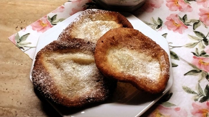 Kniek&uuml;chle liegen auf einem Teller, leicht best&auml;ubt mit Puderzucker, auf einem dekorativen Tischunterlage mit Blumen.