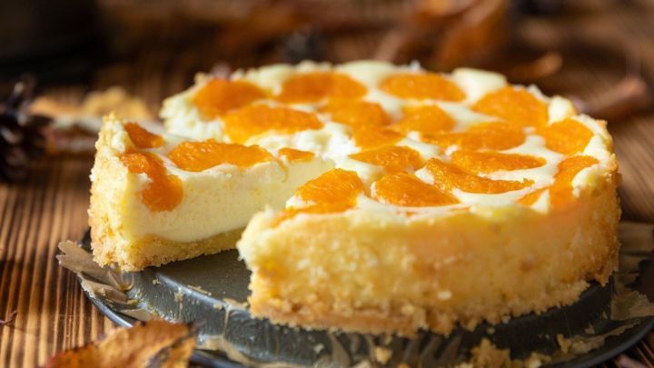 Ein Mandarinen-Schmand-Kuchen mit einer cremigen oberen Schicht und Mandarinenst&uuml;cken auf einem rustikalen Holzuntergrund.