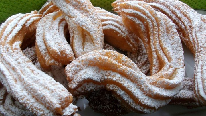 Frittierte Churros liegen auf einem Teller, best&auml;ubt mit Puderzucker, vor einer gr&uuml;nen Textilunterlage.