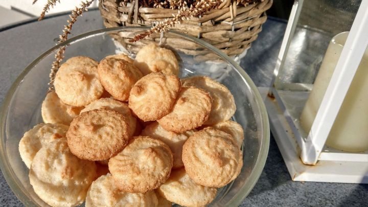 Weiche Kokosmakronen liegen in einer Glassch&uuml;ssel, umgeben von einem hellen Tisch und einem dekorativen Korb.