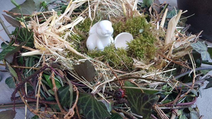 Ein festlich dekoriertes Osternest aus Zweigen, Heu und Moos, in der Mitte sitzt ein kleiner wei&szlig;er Hase.