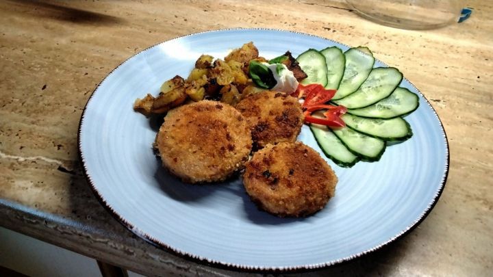 Auf einem Teller liegen panierte G&ouml;ttinger W&uuml;rste, die knusprig gebraten sind, neben Bratkartoffeln und frischem Gem&uuml;se.