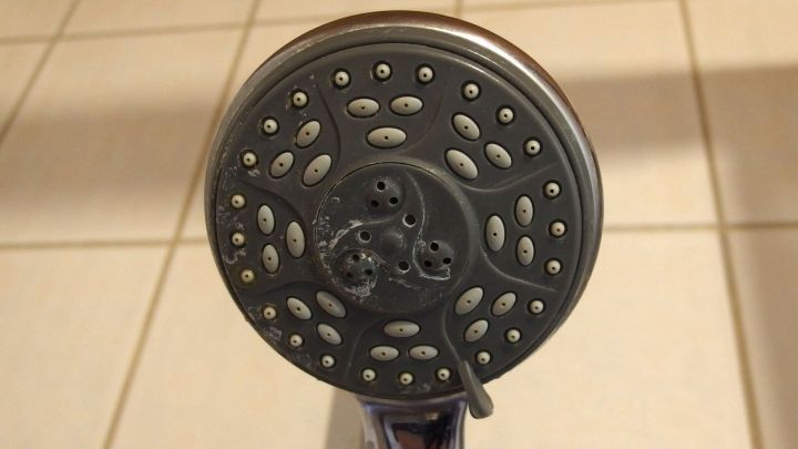 Der Brausekopf ist durch Kalkablagerungen grau gef&auml;rbt, w&auml;hrend er in einer eleganten Badezimmerumgebung befestigt ist.