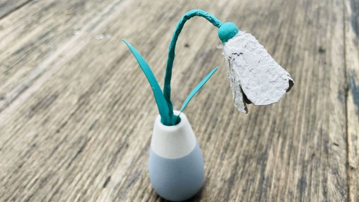 Ein Schneegl&ouml;ckchen aus Eierkarton steht in einer Vase und zeigt Bl&uuml;ten und Bl&auml;tter, umgeben von einer Holzoberfl&auml;che.