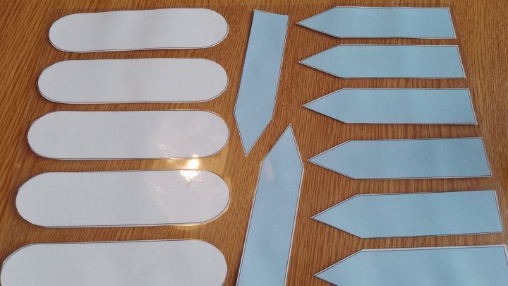 Wei&szlig;e Pflanzenschilder liegen auf einer Holzoberfl&auml;che, bereit zum Beschriften und f&uuml;r den Einsatz im Garten.