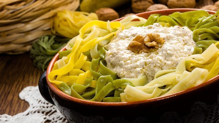 Eine Sch&uuml;ssel mit bunten Tagliatelle, umgeben von Waln&uuml;ssen, bietet einen italienischen Pasta-Klassiker mit cremigem Belag.