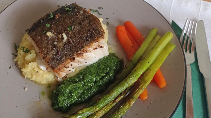 Kabeljau liegt auf cremigem Kartoffelp&uuml;ree, umgeben von gr&uuml;nem Spargel und buntem Gem&uuml;se auf einem Teller.