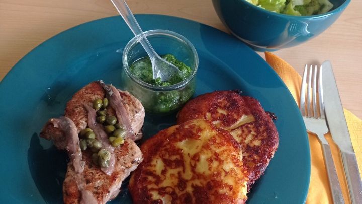 Saftiges Kalbsfilet liegt neben knusprigen Kartoffelpuffern auf einem blauen Teller, umgeben von einem frischen Salat.