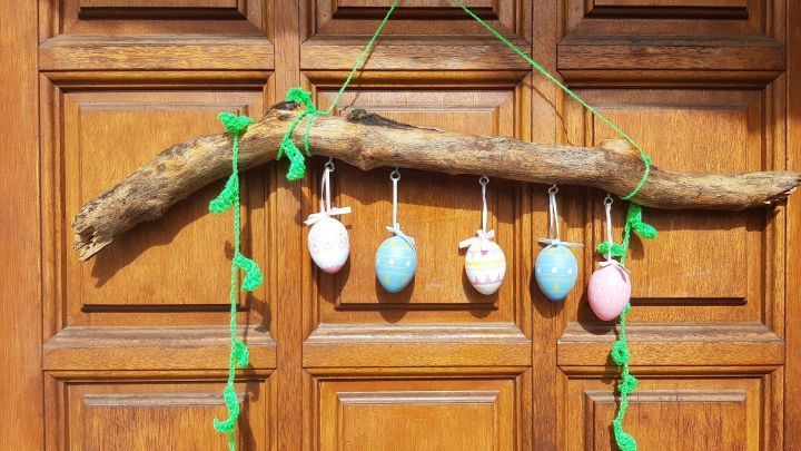 Ein sch&ouml;nes Holzst&uuml;ck h&auml;ngt an einer T&uuml;r, dekoriert mit bunten Ostereiern und gr&uuml;nen F&auml;den, um Fr&uuml;hlingsstimmung zu verbreiten.