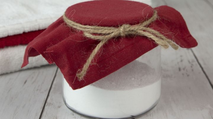 Ein Glas mit wei&szlig;em Natron ist mit einem roten Tuch abgedeckt und steht auf einem Holztisch, umgeben von frischen Blumen.