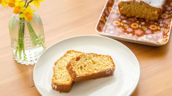Schnitten von einem saftigen Eiwei&szlig;kuchen liegen auf einem Teller, umgeben von frischen Blumen in einer Vase.