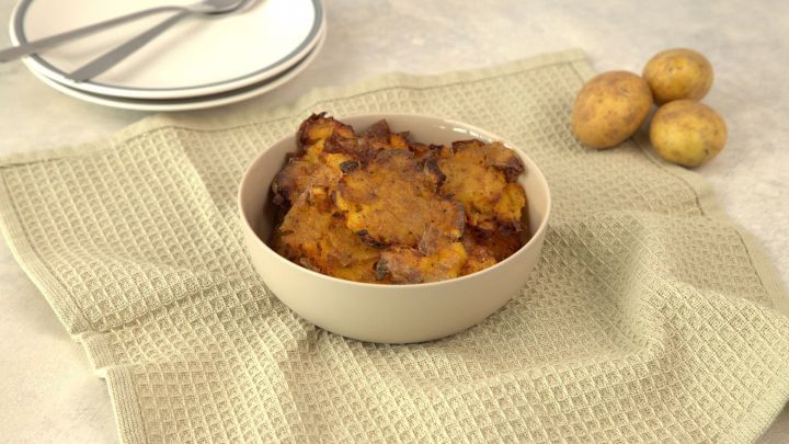 Ger&ouml;stete Quetschkartoffeln liegen in einer Sch&uuml;ssel auf einem K&uuml;chenhandtuch, umgeben von frischen Kartoffeln.