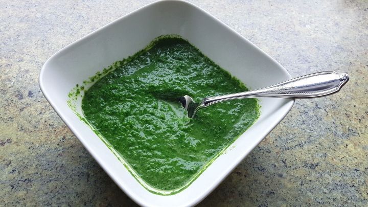 Ein tiefgr&uuml;ner Brennnesselspinat befindet sich in einer wei&szlig;en Sch&uuml;ssel, daneben liegt ein silberner L&ouml;ffel.