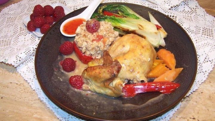 Eine goldbraun gebratene Maispoularde liegt auf einem Teller, umgeben von Blumenkohlreis und buntem Gem&uuml;se, angerichtet mit Beeren.