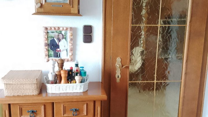 Ein Holzschrank und eine Holzt&uuml;r stehen in einem Raum. Der Schrank ist dekorativ mit Geschirr und Pflegeprodukten gef&uuml;llt.