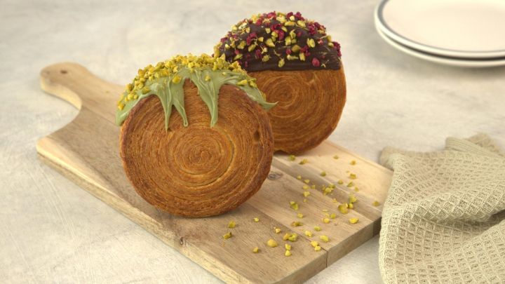 Zwei runde New York Rolls liegen auf einem Holzbrett, einer mit gr&uuml;nem und der andere mit dunkler Schokolade verziert.