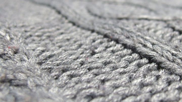 Grauer Strickstoff mit sichtbaren Fusseln und Knoten, der eine unebene Struktur zeigt und zum Kleidungsst&uuml;ck geh&ouml;rt.